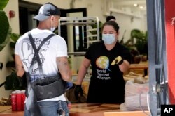 Volunteer Karla Hoyos hands out meals from the Red Rooster Overtown restaurant during the new coronavirus pandemic in Miami, March 30, 2020. Chef Marcus Samuelsson loaned his as-yet-unopened Red Rooster Overtown restaurant to chef Jose Andres' staff.