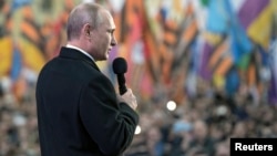 Russian President Vladimir Putin addresses the audience during a festive concert marking the first anniversary of the Crimean treaty signing, with St. Basil's Cathedral seen in the background, in central Moscow, March 18, 2015. 