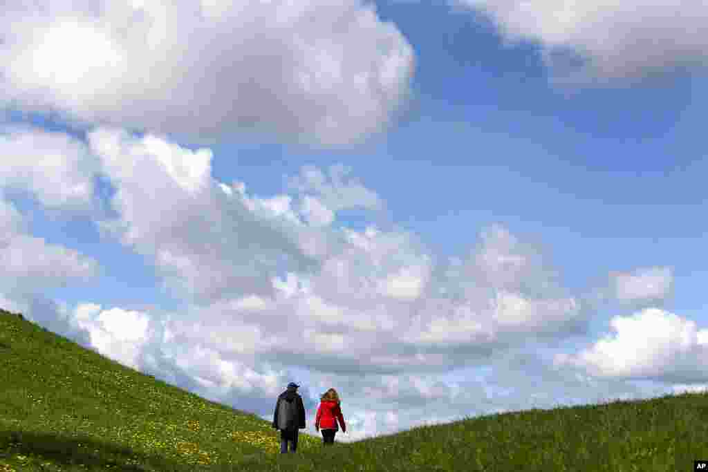 A couple walks up a hill while clouds hang over the Olympic park in Munich, Germany.