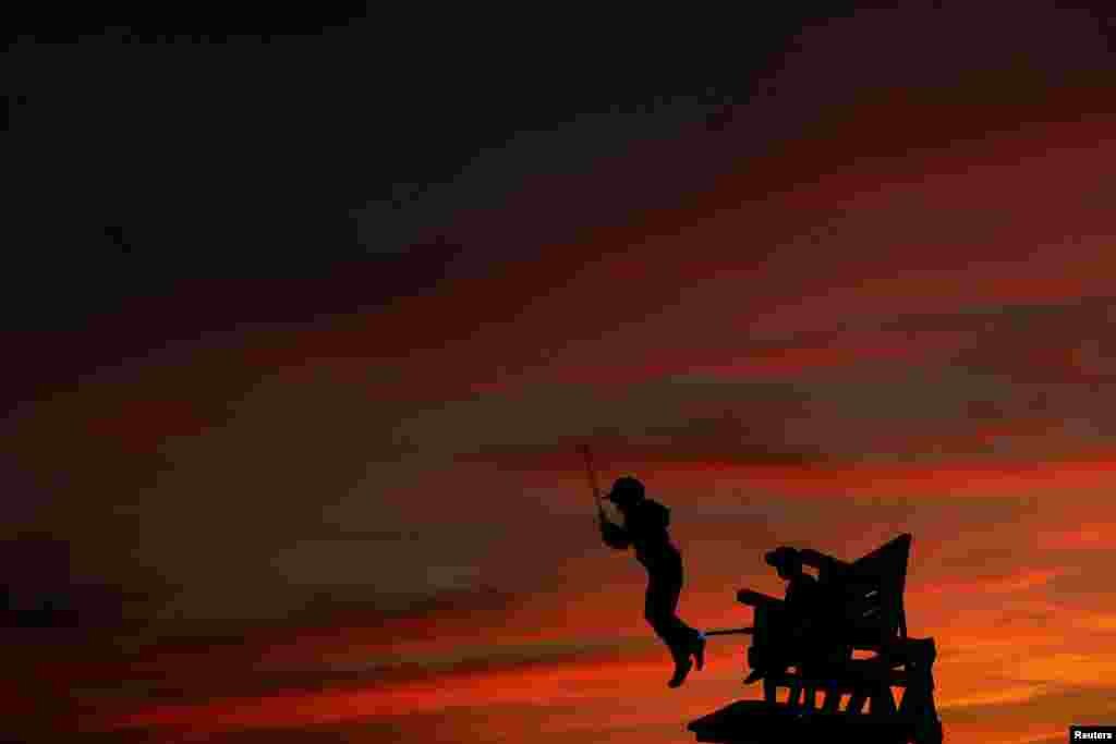A boy is seen in silhouette jumping off a lifeguard stand at Atlantic Beach, New York, July 2, 2017.