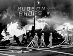 FILE - In this Aug. 14, 1965 file photo, firefighters battle a blaze set in a shoe store that collapses in flames during rioting in the Watts district of Los Angeles.