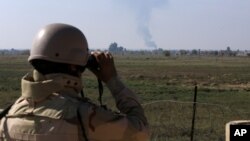 Seorang tentara Irak mengamati asap yang membumbung setelah serangan udara dari jet tempur koalisi internasional yang dipimpin AS terhadap ISIS di perbatasan Suriah-Irak di Qaim, Provinsi Anbar, Irak. (Foto: AP)