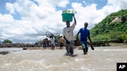FILE - People cross a river with their belongings where a bridge once stood in Phaloni, Southern Malawi, Jan 22, 2015. 