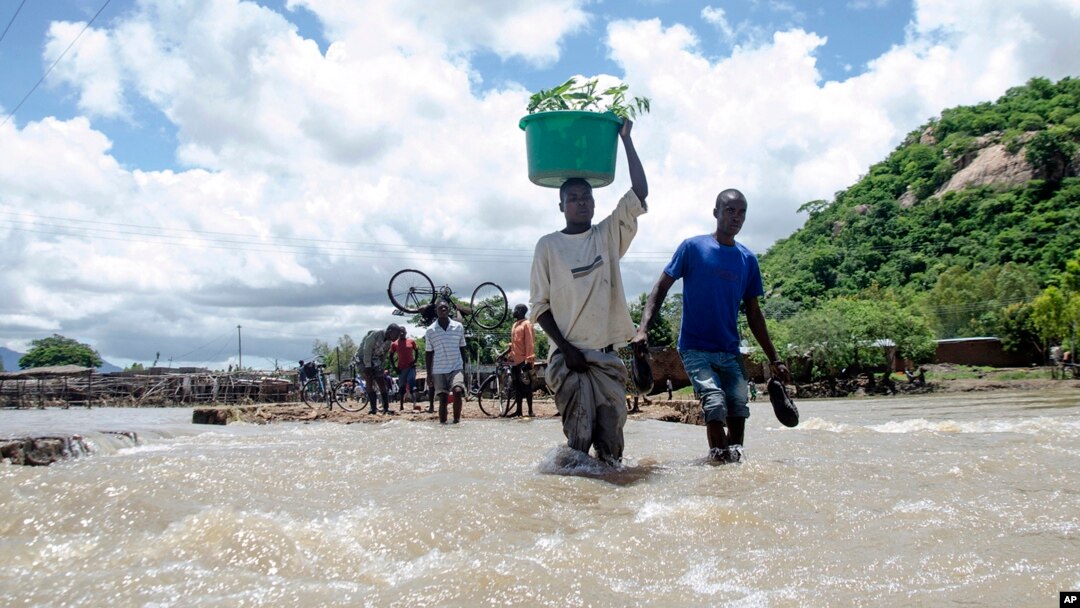 FILE - People cross a river with their belongings where a bridge once stood in Phaloni, Southern Malawi, Jan 22, 2015. 