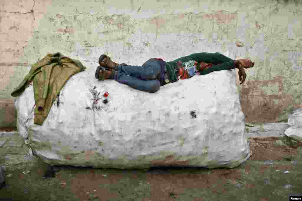 A rag picker takes a nap on a sack filled with used plastic bottles, on the side of a road in New Delhi, India.