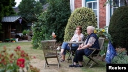 Dua perempuan lansia duduk di taman di depan rumah mereka di Wacken, Jerman, 2 Agustus 2019. (Foto: Reuters)