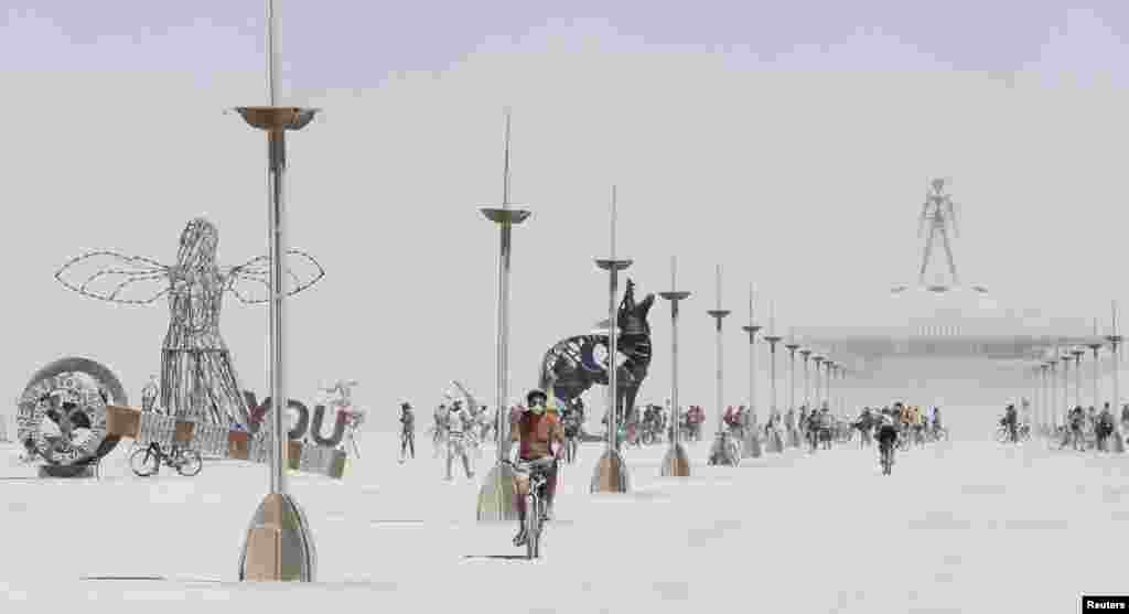 A participant bicycles away from the effigy of the Man (R, top) at the 2013 Burning Man arts and music festival in Black Rock Desert, Nevada, USA, Aug. 29, 2013. The federal government issued a permit for 68,000 people from all over the world to gather at the sold out festival, which is celebrating its 27th year, to spend a week in the remote desert to experience art, music and the unique community.
