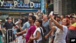 FILE - A New York police officer stands watch as visitors stage selfies for a giant monitor playback in Times Square in New York City, July 3, 2015.