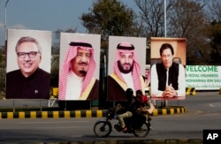 Pakistani riders drive past portraits of Pakistani and Saudi leaders displayed in Islamabad, Pakistan, Feb. 15, 2019.