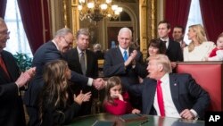 Le président Donald Trump entouré de sa famille et des dirigeants du Congrès, donne une poignée de main avec le chef de la minorité du Sénat, Charles Schumer, de NY, après avoir signé formellement la nomination des membres de son cabinet, vendredi 20 janvier 2017