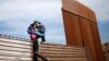 Seorang pria migran tampak melompati pagar perbatasan Meksiko-AS sambil membawa seorang putrinya, dalam upaya masuk wilayah AS secara ilegal dari Tijuana, Meksiko (foto: ilustrasi). 