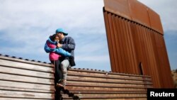 Seorang pria migran Honduras, dengan menggendong putrinya berusaha masuk wilayah AS secara ilegal dengan memanjat pagar perbatasan AS-Meksiko dari kota Tijuana, Meksiko (12/12).