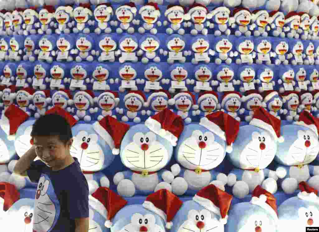 A boy wearing a Doraemon t-shirt stands in front of a Christmas tree made up of Japanese Manga character Doraemon at a shopping mall in the central business district in Singapore.