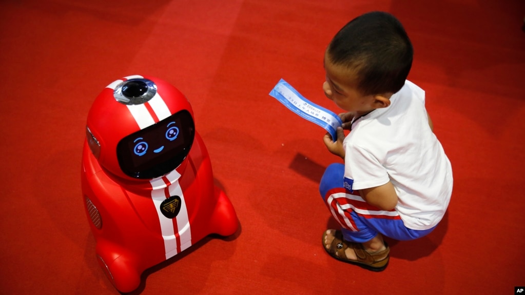 Một em bé cầm vé vào cửa ngồi nhìn môt robot tự học tinh khôn tại Hội nghị Robot Thế giới 2017 ở Bắc Kinh, ngày 23/8/2017.