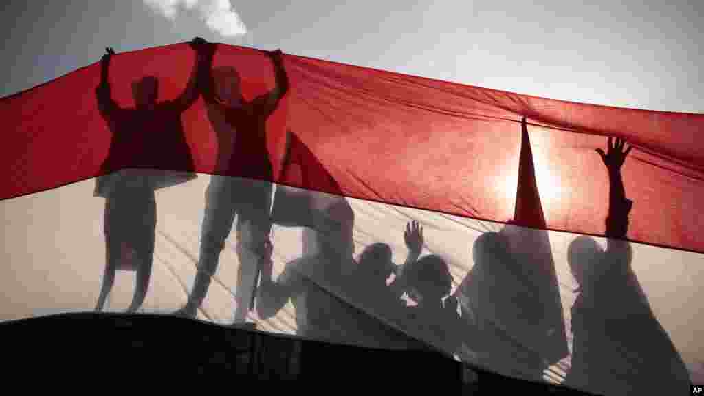 Men are silhouetted against a large representation of the Yemeni flag as they attend a ceremony to mark the 54th anniversary of North Yemen&#39;s revolution in Sana&#39;a.