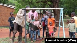 As children wait their turn on a swing set, Kanduwa Sande give one a push. (Lameck Masina/VOA)