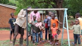 As children wait their turn on a swing set, Kanduwa Sande give one a push. (Lameck Masina./VOA)