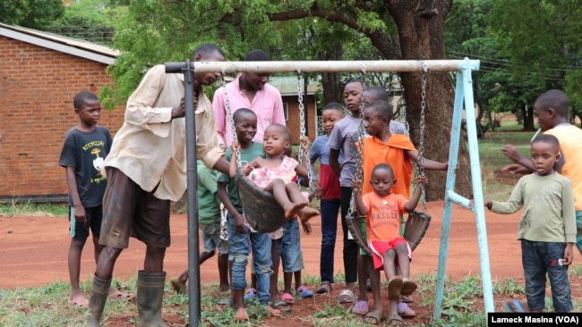 As children wait their turn on a swing set, Kanduwa Sande give one a push. (Lameck Masina./VOA)