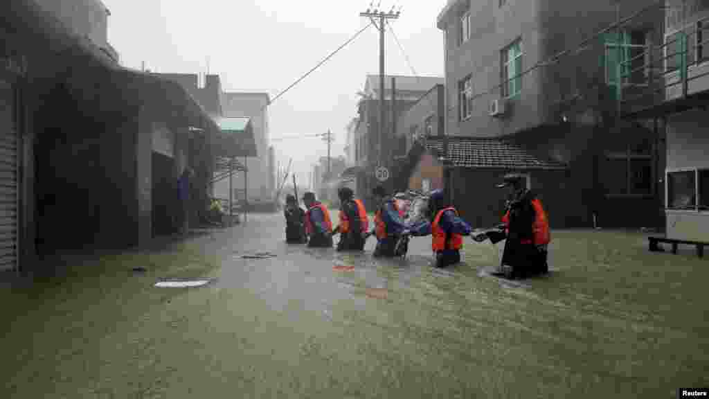Des secouristes se tiennent les mains et marchent en file dans une rue inondée d&#39;une ville chinoise à la recherche des victimes, 9 août 2015