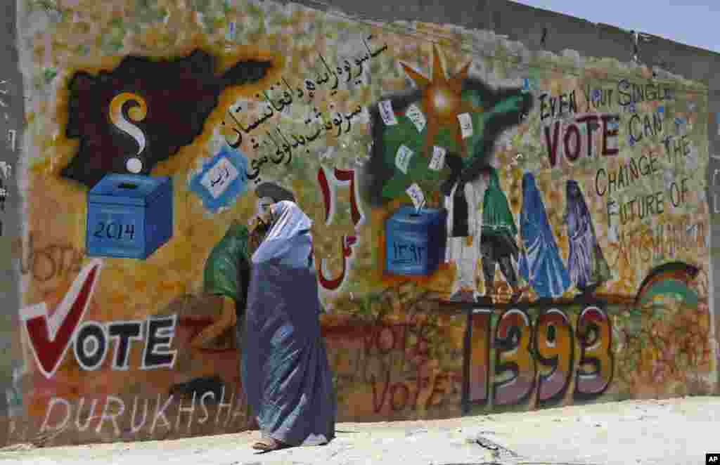 A woman walks past a mural to support voting in Kandahar, south of Kabul, June 13, 2014.&nbsp;