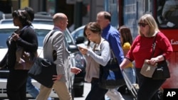 FILE- In this photo taken Wednesday, June, 29, 2010, a woman text messages while walking across the street in San Francisco. Beginning on October 24, you could be fined from $15 to $99 if you step into a Honolulu street while looking at your phone.