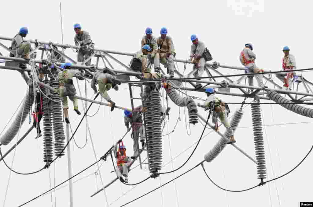 Workers climb onto equipment to perform maintenance work at an electric power transformation substation in Xuzhou, Jiangsu province, China.