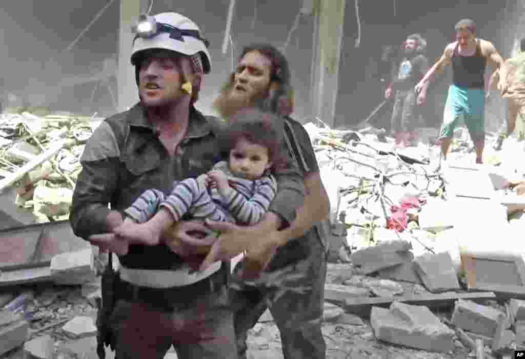 In this image made from video and posted online from Validated UGC, a civil defense worker carries a child after airstrikes hit Aleppo, April 28, 2016.