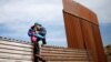 Seorang pria migran dari Honduras tampak melompati pagar perbatasan Meksiko-AS sambil membawa seorang putrinya, dalam upaya masuk wilayah AS secara ilegal dari Tijuana, Meksiko.