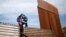Seorang pria migran dari Honduras tampak melompati pagar perbatasan Meksiko-AS sambil membawa seorang putrinya, dalam upaya masuk wilayah AS secara ilegal dari Tijuana, Meksiko.