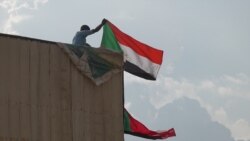 A man climbed a billboard in Khartoum to wave Sudan’s flag in honor of the agreement signing (E. Sarai/VOA)