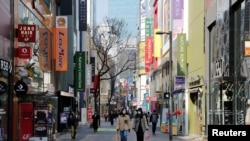 Women, wearing masks to prevent contracting COVID-19 following the outbreak of the coronavirus disease, walk in a shopping district in Seoul, South Korea, March 23, 2020.