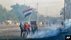 Para pemrotes membawa bendera nasional Irak saat petugas keamanan menembakkan gas air mata di pusat kota Baghdad, Irak, 20 Januari 2020.