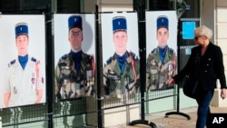 A woman looks at portraits of French soldiers killed in the helicopter collision fighting Islamic State group-linked extremists in Mali, Nov. 27, 2019.