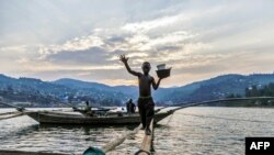 Izabayo, 13 ans, marmites d’une main, débarque d’un bateau de pêche en se balançant sur un pont en tronc d’arbre sur les eaux du lac Kivu, 17 juillet 2017.