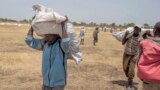 South Sudanese men carry food distributed by the World Food Program in Leer County Southern Leich State in South Sudan, March 6, 2017.