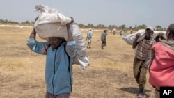 South Sudanese men carry food distributed by the World Food Program in Leer County Southern Leich State in South Sudan, March 6, 2017.