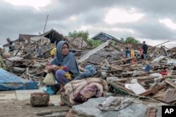 A tsunami survivor sits on debris as she salvages items from the location of her house in Sumur, Indonesia, Dec. 24, 2018.