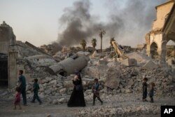 FILE - Iraqi civilians are seen walking past the destroyed al-Nuri mosque in the Old City of Mosul, Iraq, July 4, 2017.