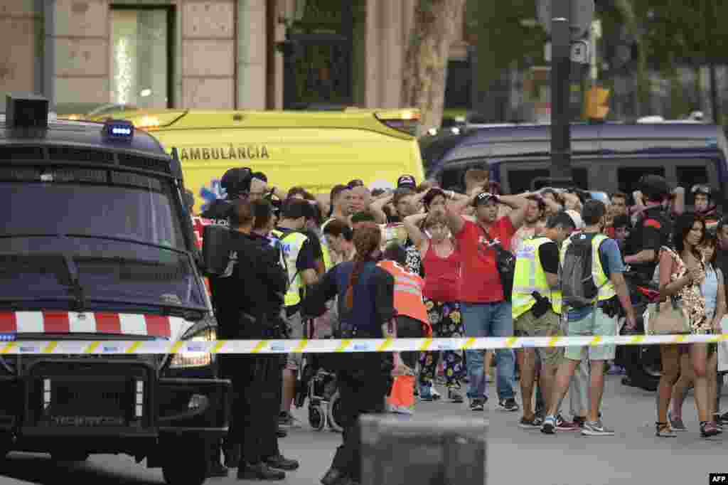 Policemen check the identity of people standing with their hands up after a van plowed into a crowd on the Las Ramblas avenue in Barcelona, Aug. 17, 2017. 
