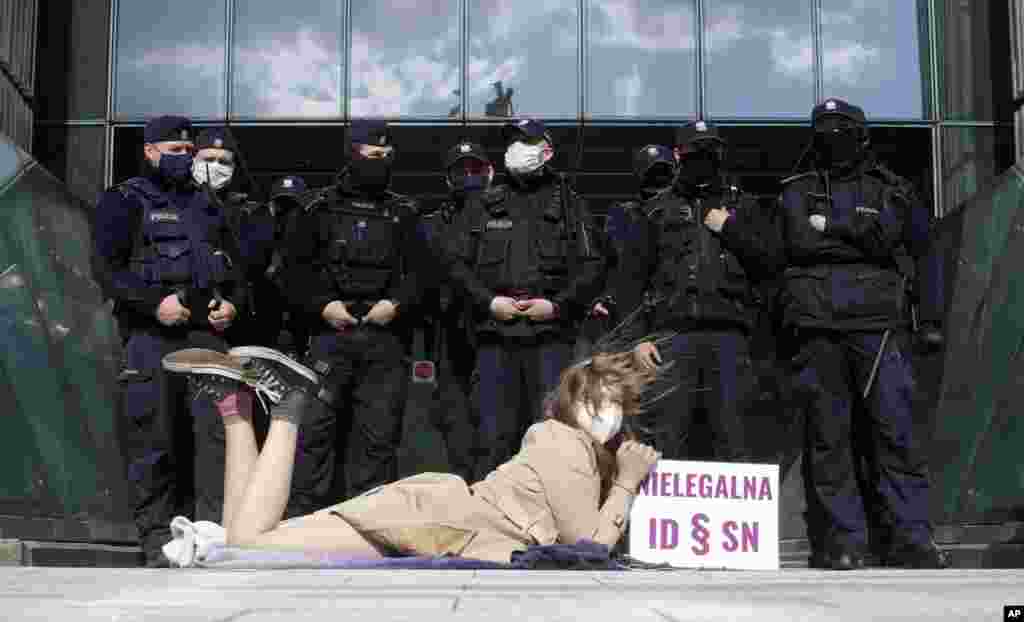 Policemen guard Poland's Supreme Court as a protester lies on the pavement in Warsaw. A disputed disciplinary body in the country's Supreme Court is examining a motion that could result in an arrest of a judge who has become a symbol of the fight for an independent judiciary. 
