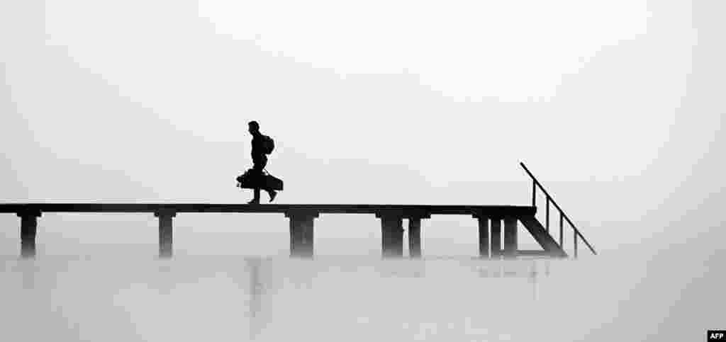 A man walks on a pier in heavy fog at lake Ammersee in Stegen, southern Germany.