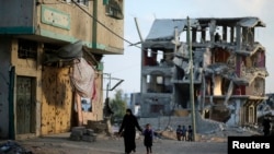 A Palestinian woman walks with her daughter as the remains of a house that witnesses said was destroyed during the 50-day war between the Hamas militant movement and Israel, in the east of Gaza City, Oct. 12, 2014.