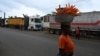 A woman selling carrots walks past trucks from Mali and Burkina Faso as they wait to load goods in the industrial area near Abidjan, Jan. 30, 2025, a day after Burkina Faso, Mali and Niger officially left the Economic Community of West African States, commonly known as ECOWAS.