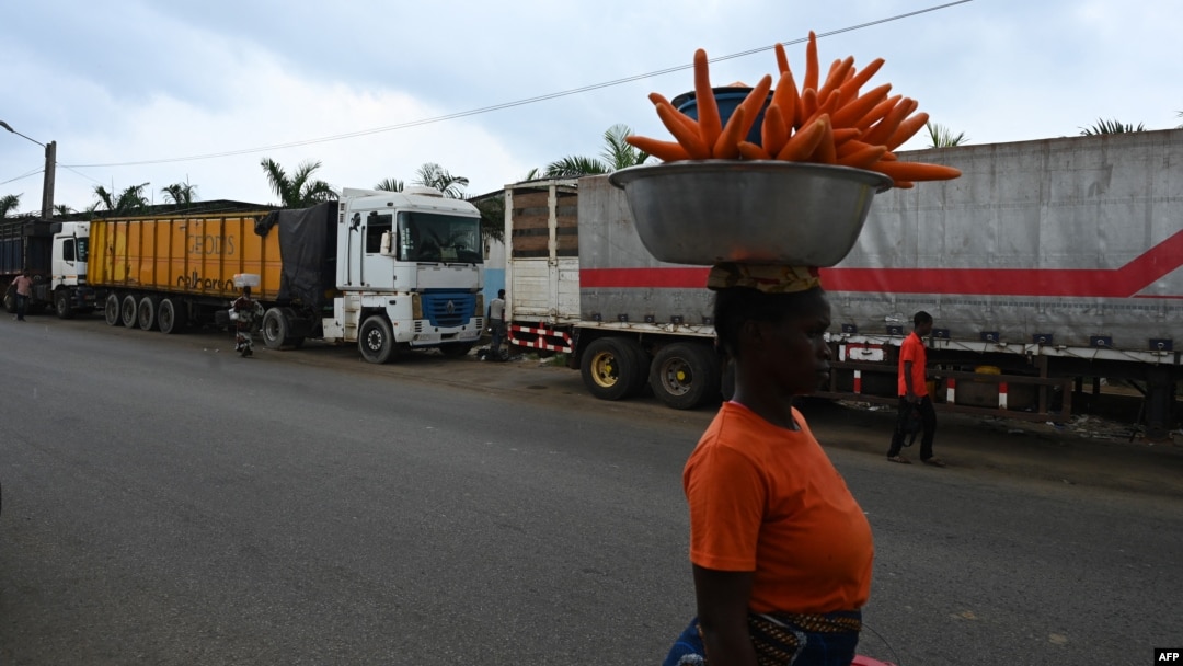 A woman selling carrots walks past trucks from Mali and Burkina Faso as they wait to load goods in the industrial area near Abidjan, Jan. 30, 2025, a day after Burkina Faso, Mali and Niger officially left the Economic Community of West African States, commonly known as ECOWAS.