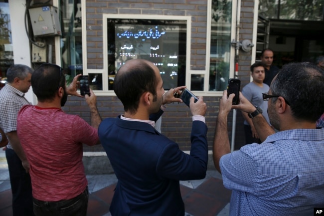 FILE - Iranians take pictures of an exchange shop screen showing various currency rates in downtown Tehran, Oct. 2, 2018. Iran's currency, the rial, had unexpectedly rallied after weeks of depreciation following President Donald Trump's decision to withdraw America from Tehran's nuclear deal with world powers, sending Iranians rushing to exchange shops to cash in.