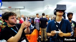 Rectal software designer Julian Kantor (L) takes a picture of Jonathan Feng (R) as he uses the Oculus Rift virtual reality headset to experience his program during E3 in Los Angeles, California June 12, 2013.