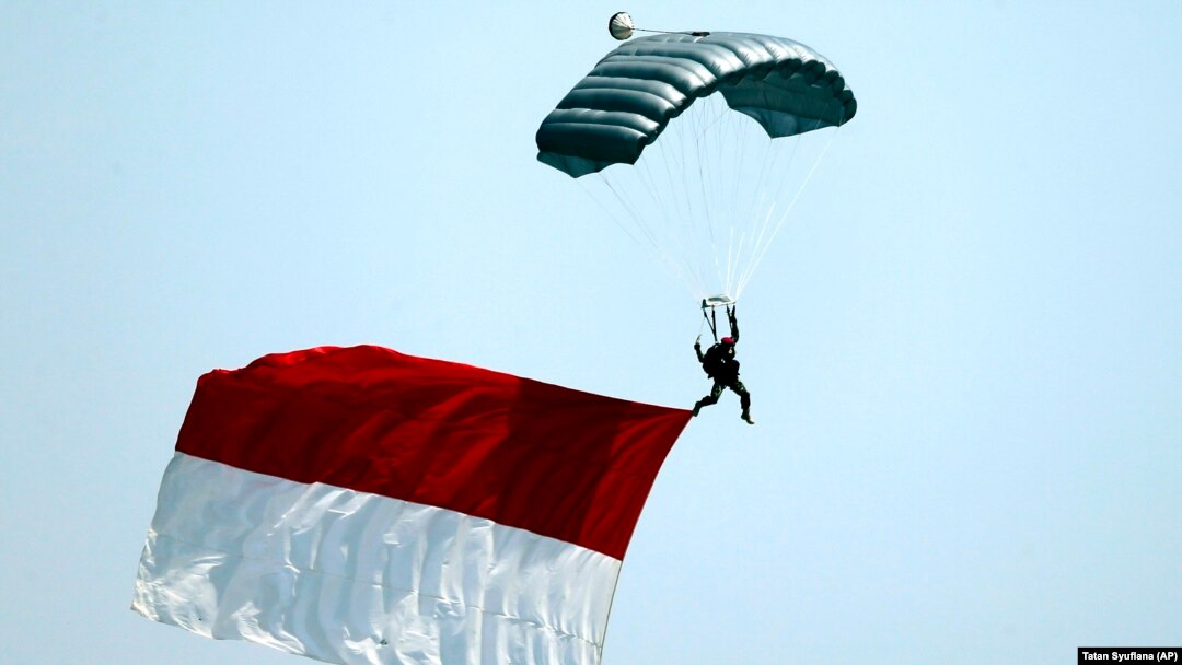 Seorang tentara melompat dengan parasut sambil membawa bendera Merah Putih dalam parade peringatan HUT ke-74 TNI, Jakarta, Sabtu, 5 Oktober 2019. (Foto: AP/Tatan Syuflana)