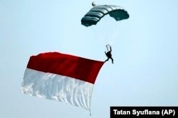 Seorang tentara melompat dengan parasut sambil membawa bendera Merah Putih dalam parade peringatan HUT ke-74 TNI, Jakarta, Sabtu, 5 Oktober 2019. (Foto: AP/Tatan Syuflana)