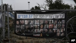 A poster shows pictures of the Bibas family, top row from second left: Yarden, Shiri, and their sons Ariel and Kfir, who were kidnapped on Oct. 7, 2023, in Jerusalem, Feb. 21, 2025. Words above read, '37 members of Kibbutz Nir Oz are still missing.'