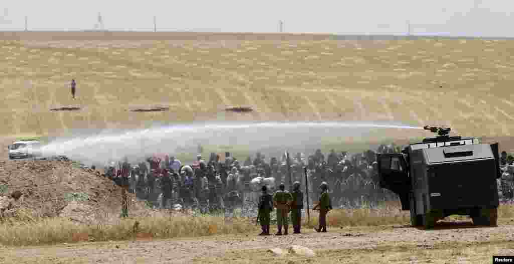 Turkish military use water cannon to stop Syrian refugees as they wait behind the border fences to cross into Turkey on the Turkish-Syrian border, near the southeastern town of Akcakale in Sanliurfa.